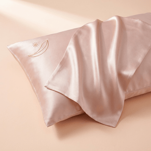 Auraclarify blush pink mulberry silk pillowcase with gold embroidered logo, draped corner showing silk sheen